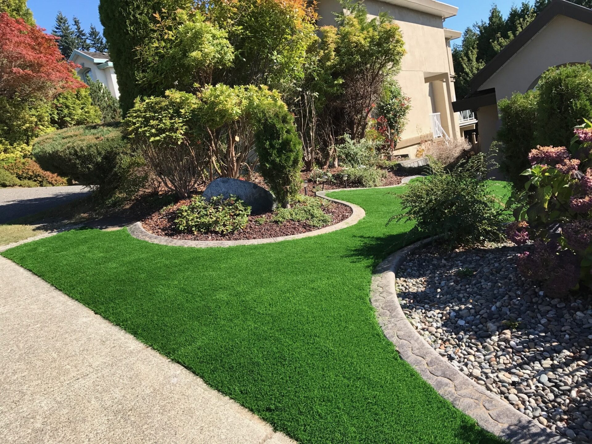 Residential landscaping with lush artificial turf lawn, decorative curbing, shrubs, and sidewalk.