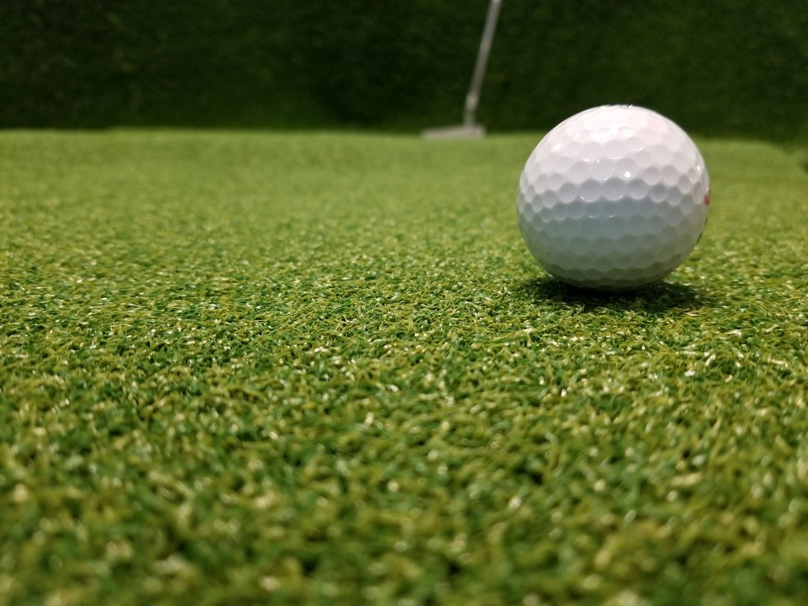 Golf ball sitting on green artificial turf putting green. Sports equipment and synthetic grass.