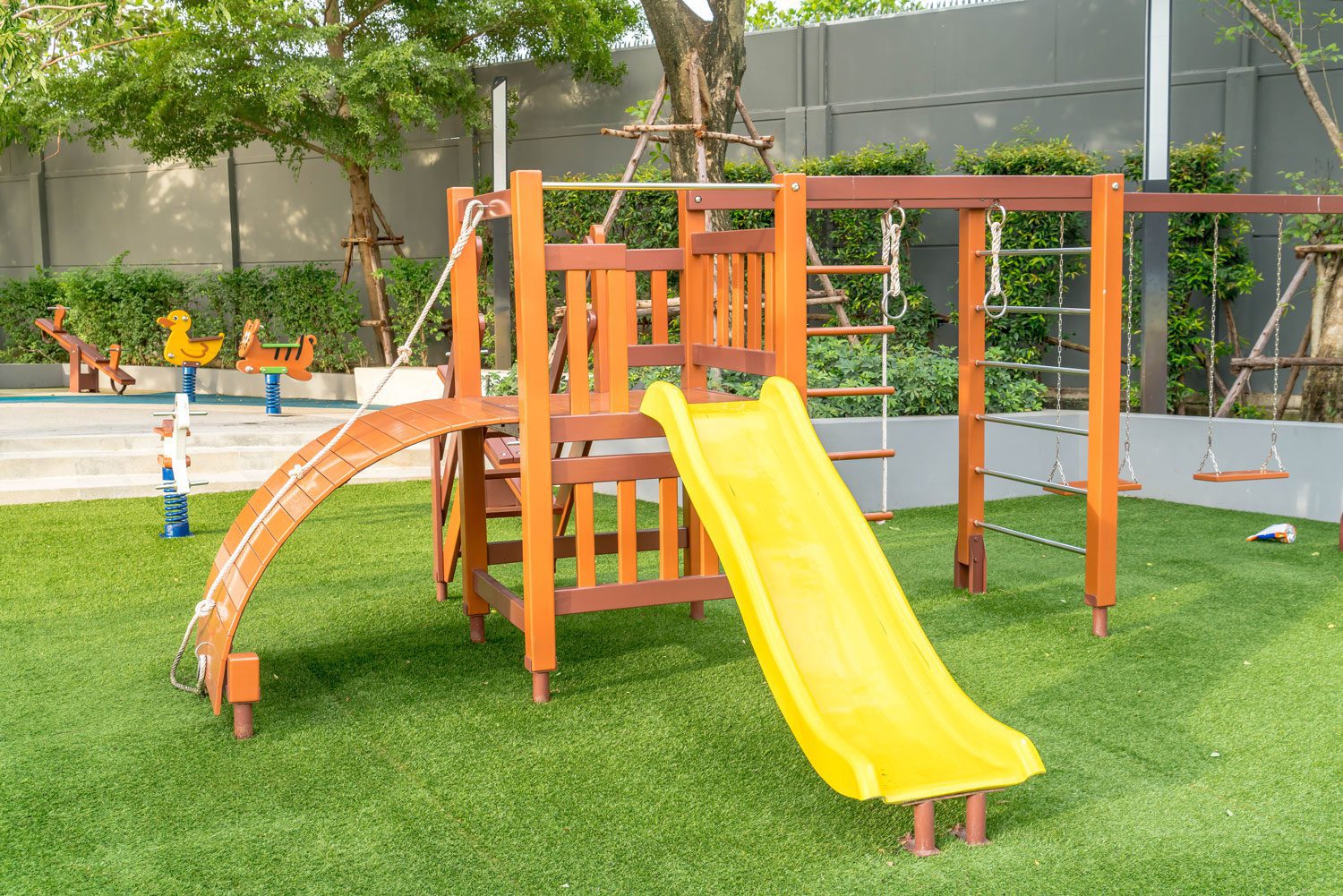 Modern playground with yellow slide, swings, climbing structure, and green artificial turf.