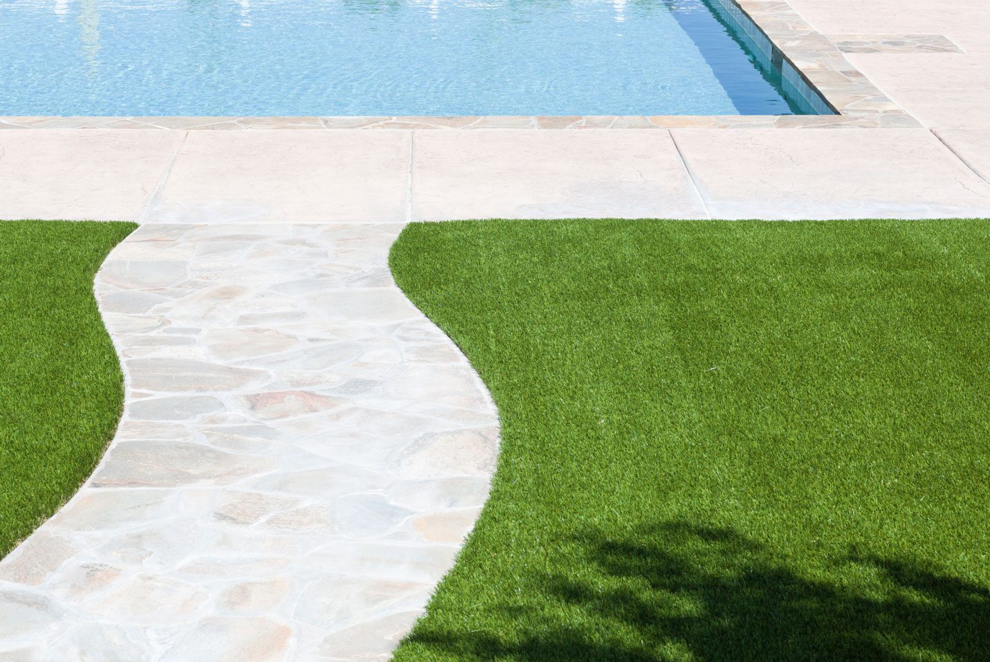 poolside Curved stone path leading to a swimming pool, bordered by bright green artificial turf.